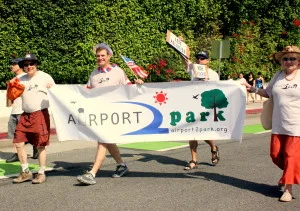 Airport2Park volunteers fly their banner as they walk the parade route. (Photo by Jason Islas)