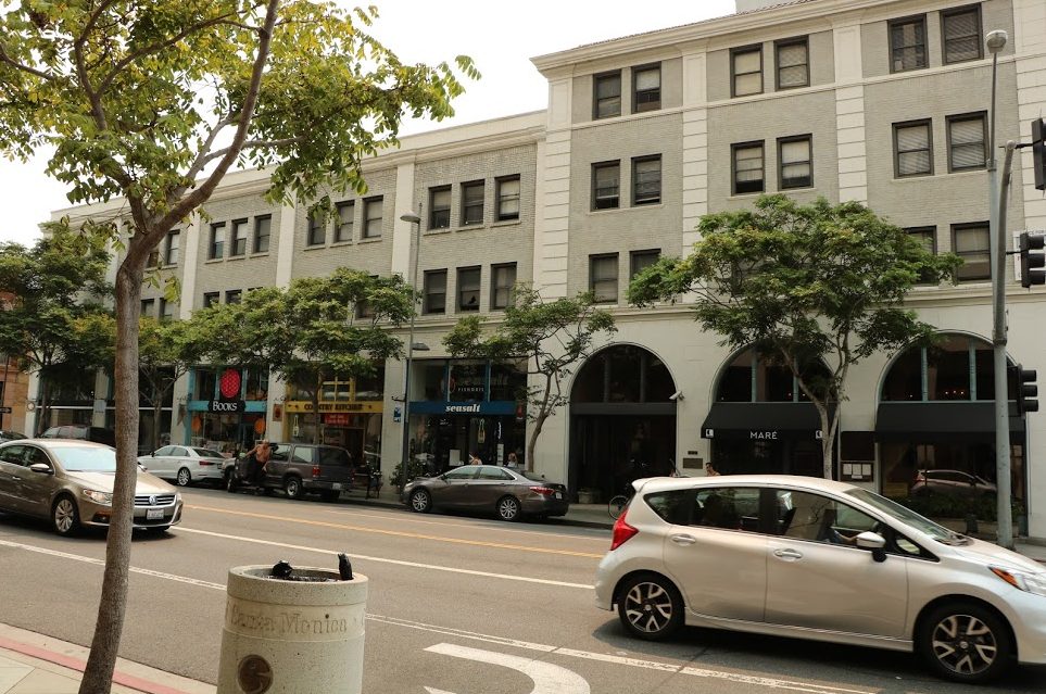 An early 20th century building at Santa Monica and 5th Street features local shops and restaurants on its ground floor, enlivening the experience for passersby.